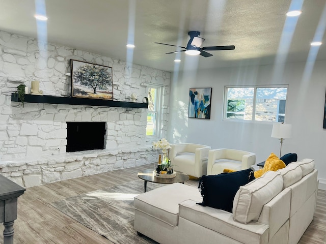 living room featuring a stone fireplace, ceiling fan, a healthy amount of sunlight, and wood-type flooring