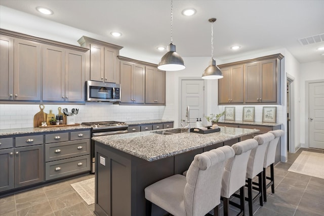 kitchen with light stone countertops, sink, pendant lighting, a center island with sink, and appliances with stainless steel finishes