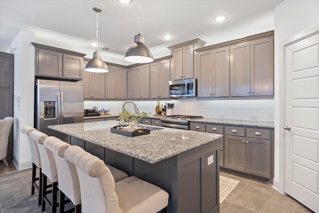 kitchen with a kitchen breakfast bar, hanging light fixtures, an island with sink, light stone counters, and stainless steel appliances