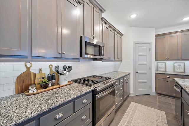 kitchen with backsplash, stone counters, dark tile patterned floors, and appliances with stainless steel finishes