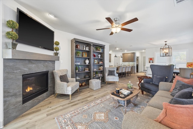 living room with a tiled fireplace, light hardwood / wood-style floors, and ceiling fan with notable chandelier