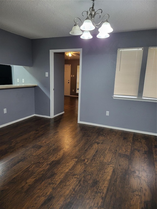 empty room with dark hardwood / wood-style floors, a textured ceiling, and ceiling fan with notable chandelier