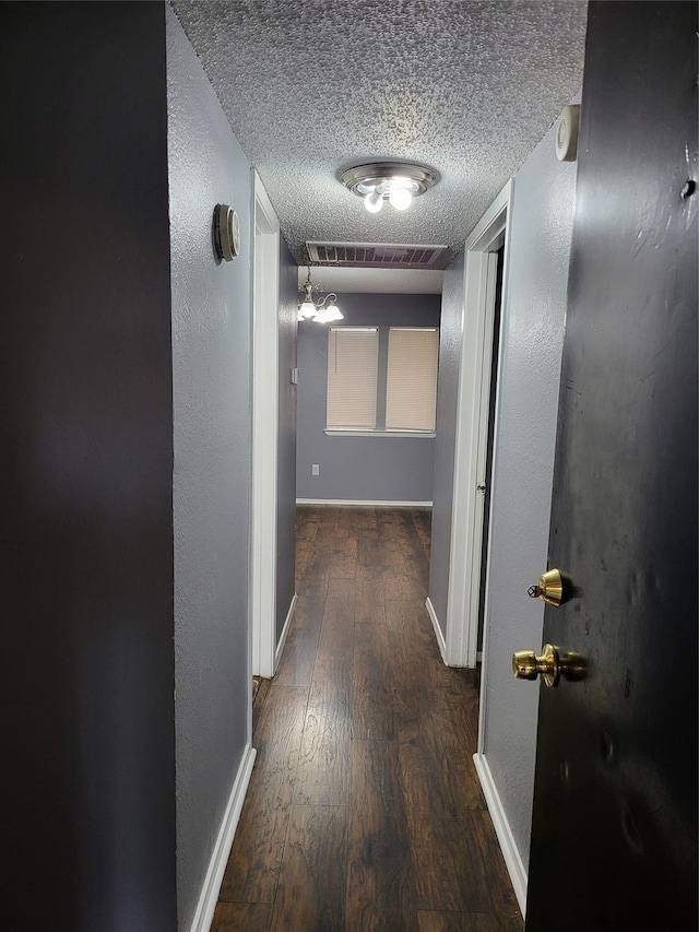 hallway featuring a notable chandelier, dark hardwood / wood-style floors, and a textured ceiling