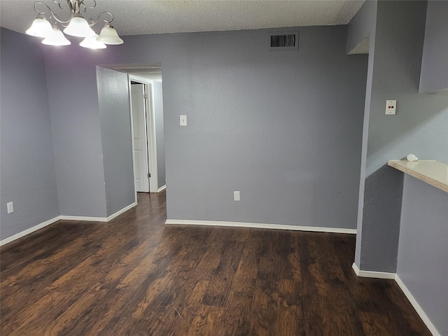 unfurnished room featuring a chandelier, a textured ceiling, and dark hardwood / wood-style floors