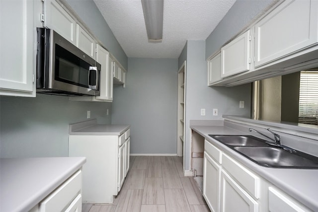 kitchen with a textured ceiling, white cabinetry, and sink