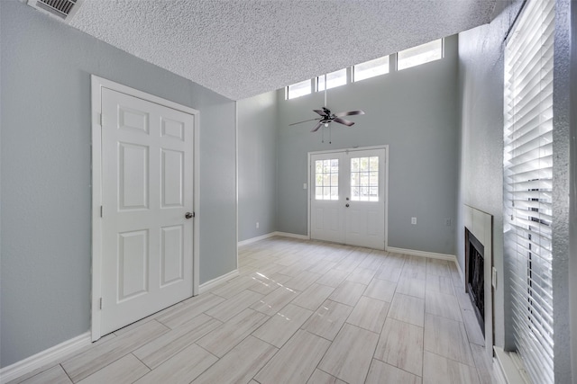 unfurnished living room with ceiling fan, a textured ceiling, a high ceiling, and french doors