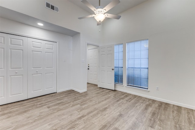 unfurnished bedroom featuring ceiling fan, a closet, a towering ceiling, and light hardwood / wood-style floors