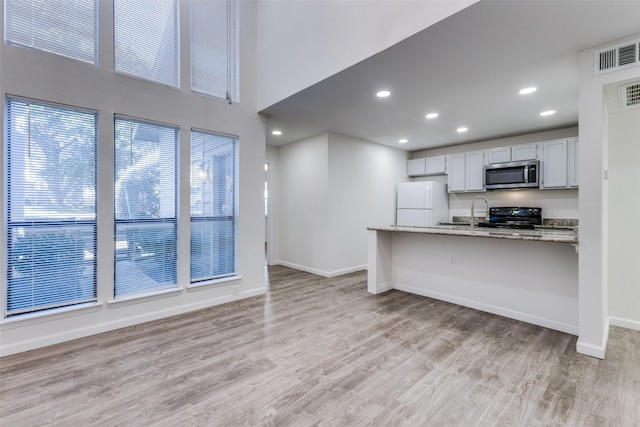 kitchen with light stone countertops, black stove, light hardwood / wood-style flooring, white fridge, and a breakfast bar area