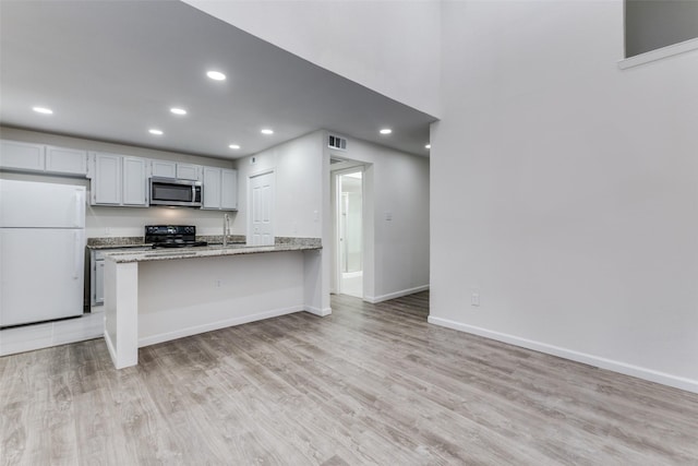 kitchen featuring a kitchen breakfast bar, light stone counters, white fridge, black range, and light wood-type flooring