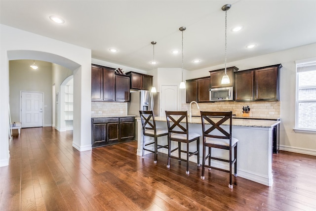 kitchen featuring backsplash, dark brown cabinetry, stainless steel appliances, pendant lighting, and an island with sink