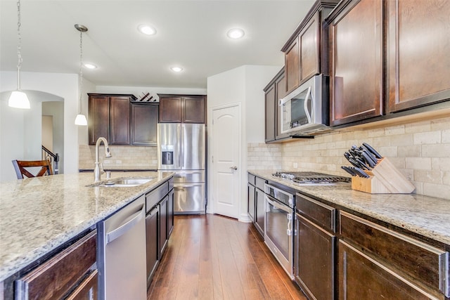 kitchen featuring sink, light stone countertops, decorative light fixtures, dark brown cabinetry, and stainless steel appliances