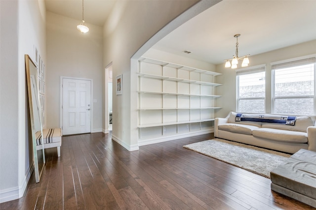 living room featuring built in features, dark wood-type flooring, a towering ceiling, and an inviting chandelier