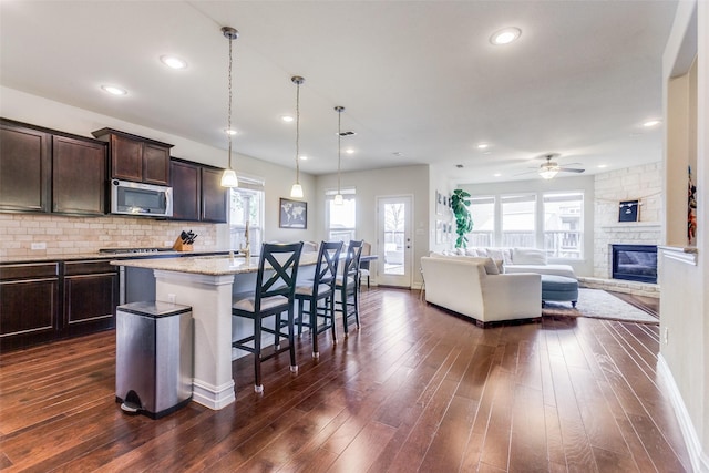 kitchen featuring dark brown cabinetry, a kitchen breakfast bar, light stone counters, backsplash, and a kitchen island with sink