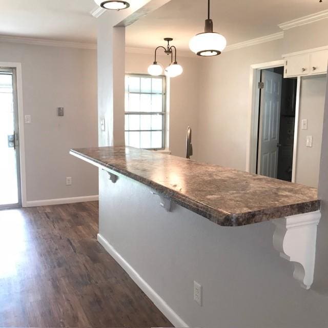 kitchen with dark countertops, a breakfast bar area, white cabinets, and crown molding