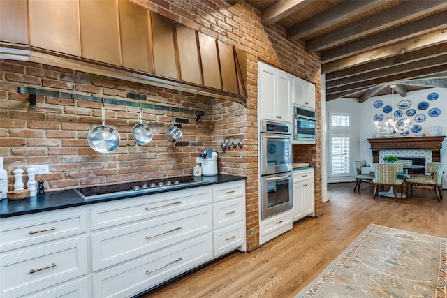 kitchen with white cabinetry, double oven, light hardwood / wood-style floors, black stovetop, and beam ceiling