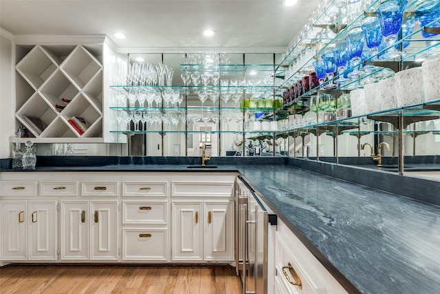 bar featuring sink, white cabinets, dark stone counters, and light hardwood / wood-style floors