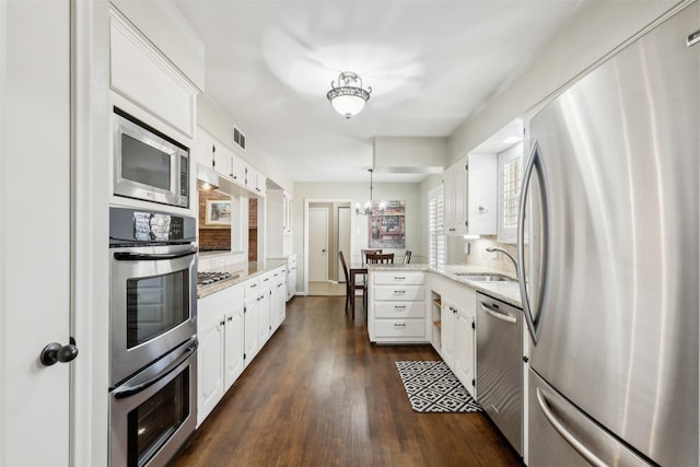 kitchen with stainless steel appliances, a notable chandelier, decorative light fixtures, white cabinets, and sink