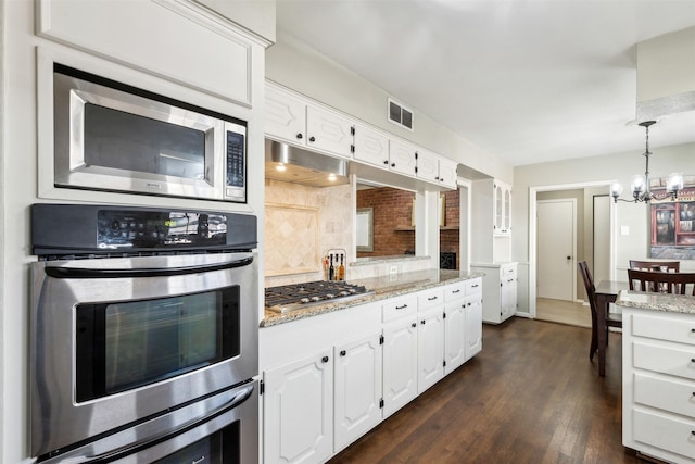 kitchen with tasteful backsplash, white cabinetry, light stone countertops, appliances with stainless steel finishes, and a chandelier