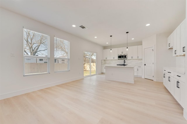 kitchen with light wood-type flooring, decorative light fixtures, white cabinetry, and an island with sink