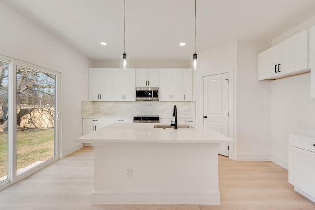 kitchen featuring white cabinetry, sink, stainless steel appliances, an island with sink, and decorative light fixtures