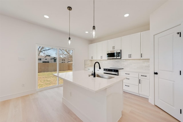 kitchen featuring appliances with stainless steel finishes, sink, decorative light fixtures, light hardwood / wood-style floors, and an island with sink