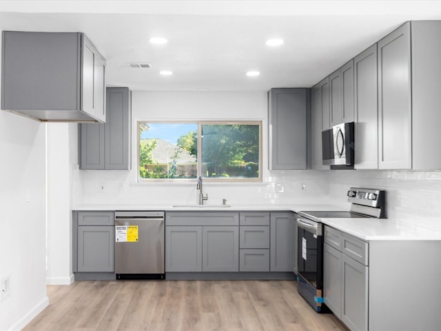 kitchen with appliances with stainless steel finishes, light wood-type flooring, gray cabinetry, and sink