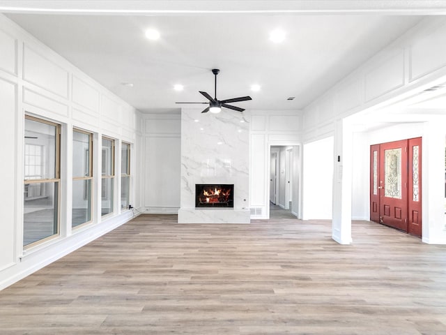 unfurnished living room with a high end fireplace, light wood-type flooring, and ceiling fan