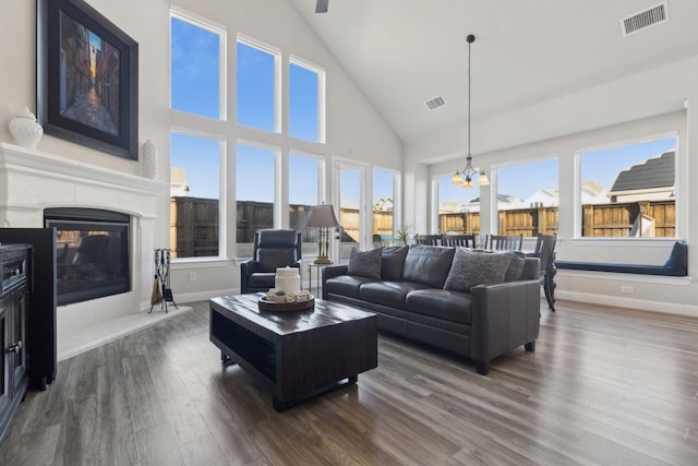 living room with a high ceiling, dark hardwood / wood-style flooring, an inviting chandelier, and plenty of natural light