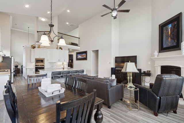 dining area with ceiling fan with notable chandelier, light hardwood / wood-style floors, and high vaulted ceiling