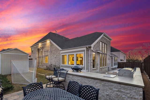 back house at dusk featuring an outdoor kitchen and a patio