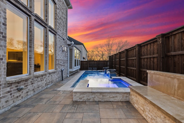 pool at dusk featuring pool water feature, a patio area, and an in ground hot tub