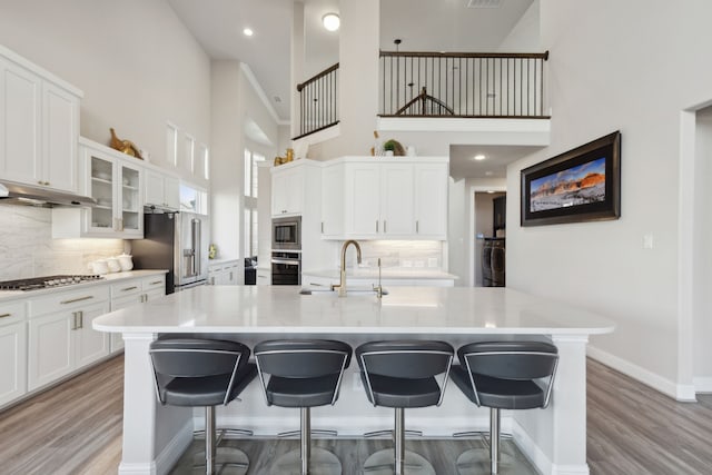 kitchen with a kitchen bar, appliances with stainless steel finishes, a kitchen island with sink, sink, and a high ceiling