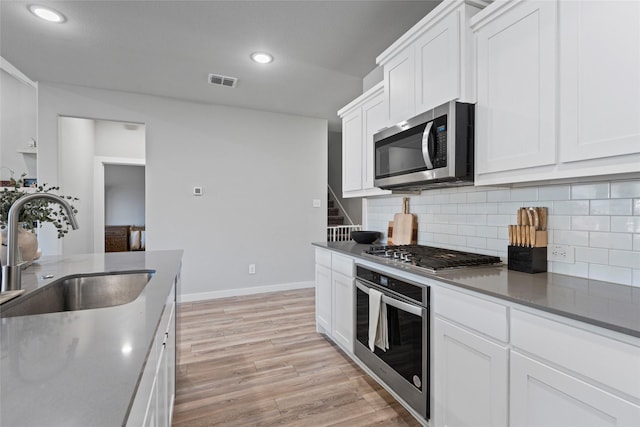 kitchen with sink, stainless steel appliances, backsplash, white cabinets, and light wood-type flooring