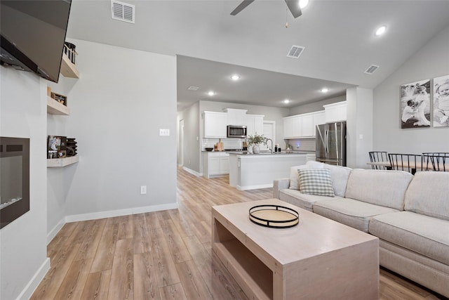 living room with light hardwood / wood-style floors, ceiling fan, lofted ceiling, and sink