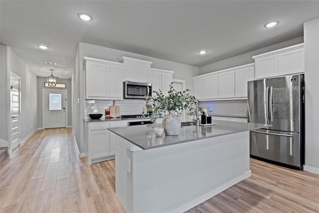 kitchen featuring white cabinets, stainless steel appliances, a center island with sink, and light hardwood / wood-style floors