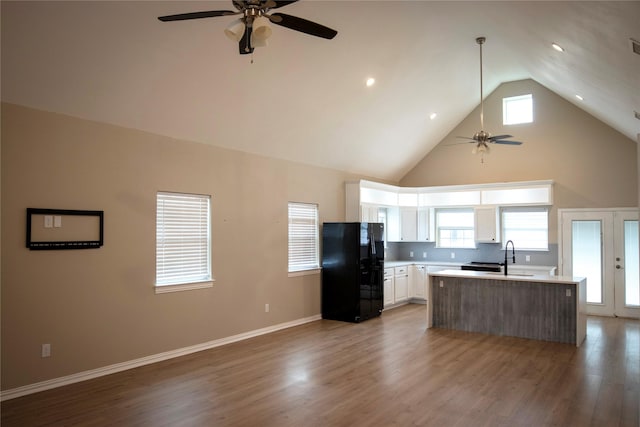 kitchen with black refrigerator, hardwood / wood-style flooring, high vaulted ceiling, a center island, and white cabinetry