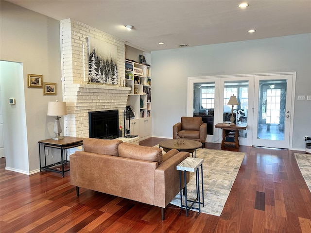 living room with built in shelves, a fireplace, and dark wood-type flooring