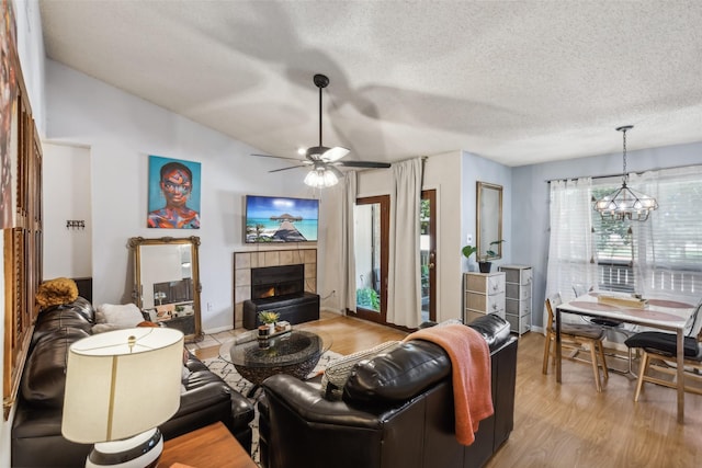 living room featuring a textured ceiling, ceiling fan with notable chandelier, light wood-type flooring, and a fireplace