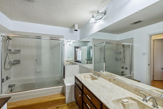 bathroom with a textured ceiling, vanity, and bath / shower combo with glass door