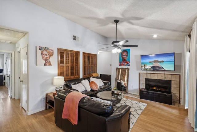 living room with a tiled fireplace, ceiling fan, light hardwood / wood-style floors, and vaulted ceiling