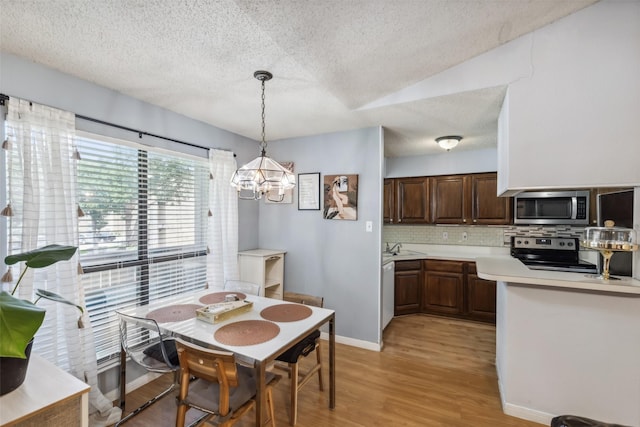 dining area with a notable chandelier, vaulted ceiling, and light hardwood / wood-style flooring