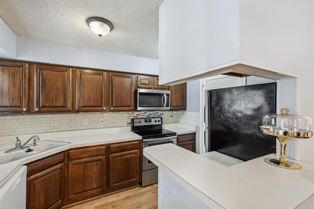 kitchen with sink, stainless steel appliances, backsplash, a textured ceiling, and light wood-type flooring