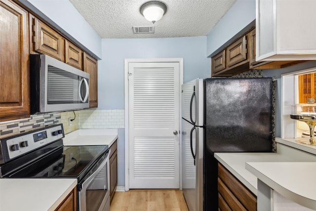 kitchen featuring tasteful backsplash, stainless steel appliances, a textured ceiling, and light hardwood / wood-style floors