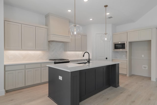 kitchen with built in microwave, sink, hanging light fixtures, an island with sink, and light hardwood / wood-style floors