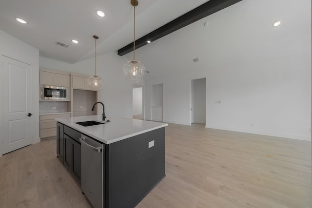 kitchen featuring a kitchen island with sink, sink, appliances with stainless steel finishes, beamed ceiling, and decorative light fixtures