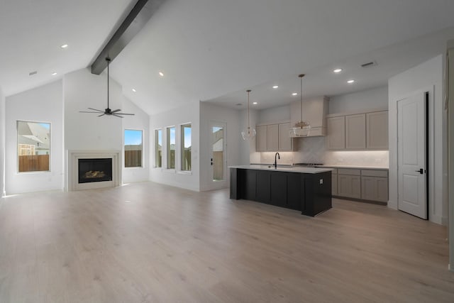 kitchen with tasteful backsplash, beam ceiling, decorative light fixtures, a center island with sink, and high vaulted ceiling