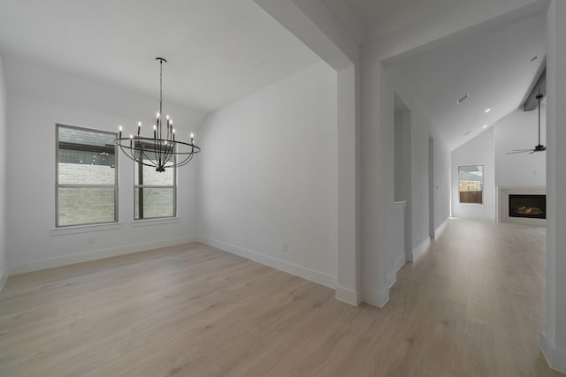 unfurnished dining area with ceiling fan with notable chandelier, light hardwood / wood-style floors, and vaulted ceiling