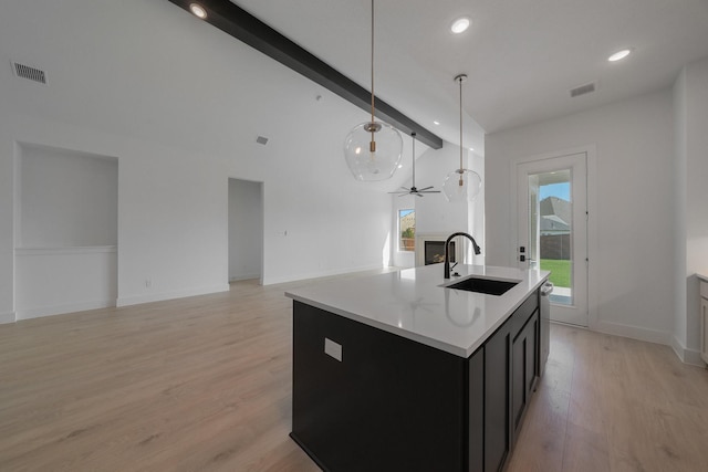 kitchen featuring light wood-type flooring, sink, decorative light fixtures, a center island with sink, and beamed ceiling