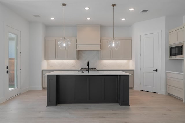 kitchen featuring light hardwood / wood-style flooring, custom range hood, an island with sink, and built in microwave