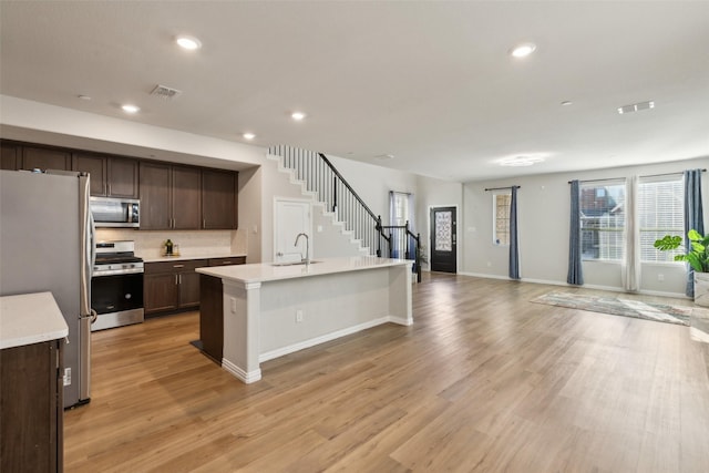 kitchen featuring a kitchen island with sink, decorative backsplash, light hardwood / wood-style floors, dark brown cabinetry, and stainless steel appliances